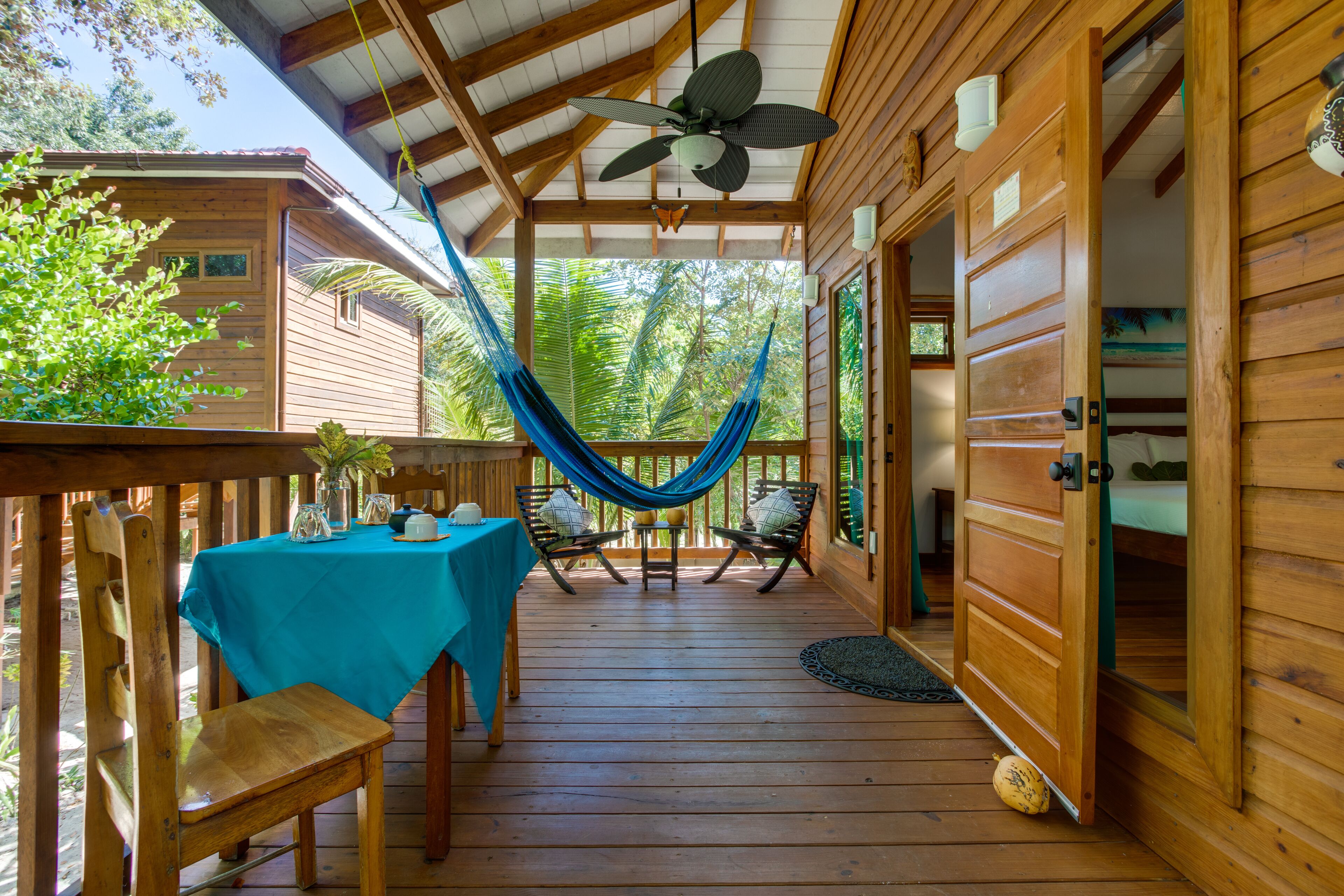 Una cabaña de madera con una hamaca, una mesa con mantel azul y un ventilador de techo.