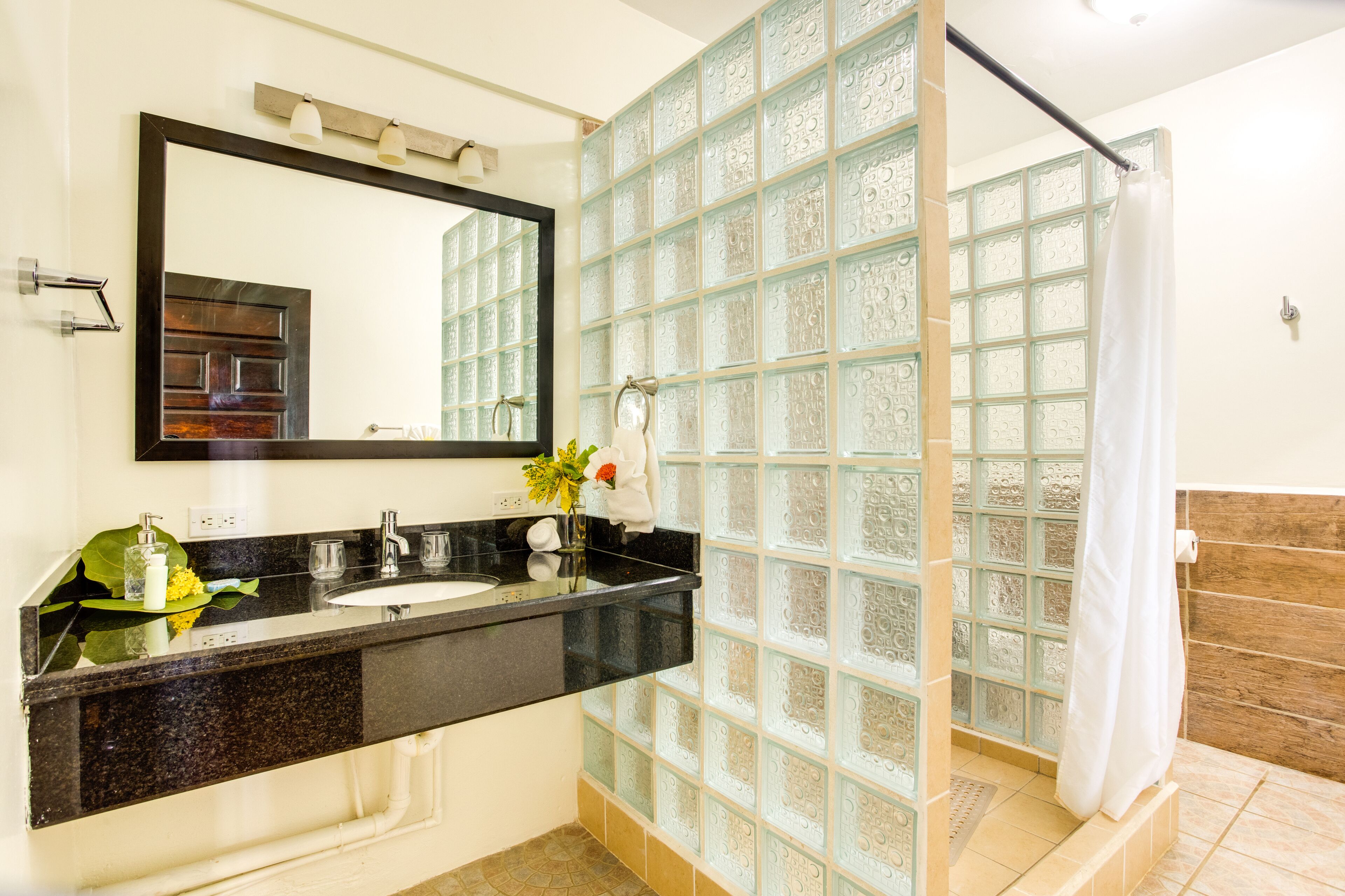 Un baño con cabina de ducha de vidrio, lavamanos con espejo y una planta decorativa.