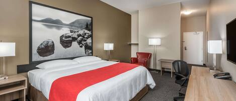 A hotel room with a large bed, a desk, a chair, and a TV.