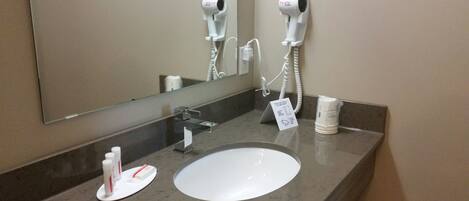 A bathroom with a sink, two hair dryers mounted on the wall, and a mirror.