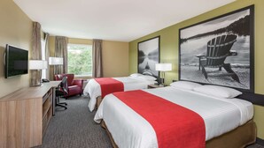Ein Hotelzimmer mit zwei Betten, einem Schreibtisch, einem Sessel, einem Fernseher und großen Fenstern.