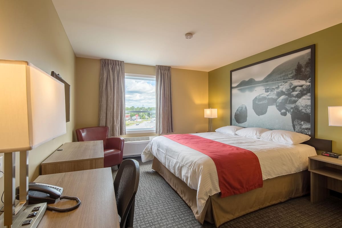 Una habitación de hotel con cama, escritorio, silla y un amplio ventanal con cortinas.