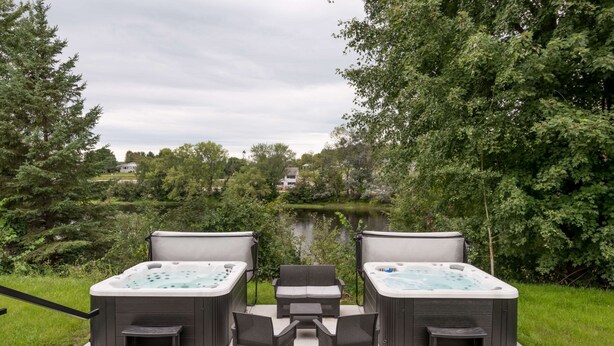 Ein Whirlpoolbereich mit zwei Whirlpools und einer Sitzecke, umgeben von Pflanzen und Blick auf einen See.