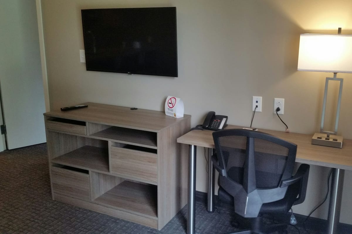 Habitación de hotel con escritorio, silla, lámpara, teléfono y televisor montado en la pared.