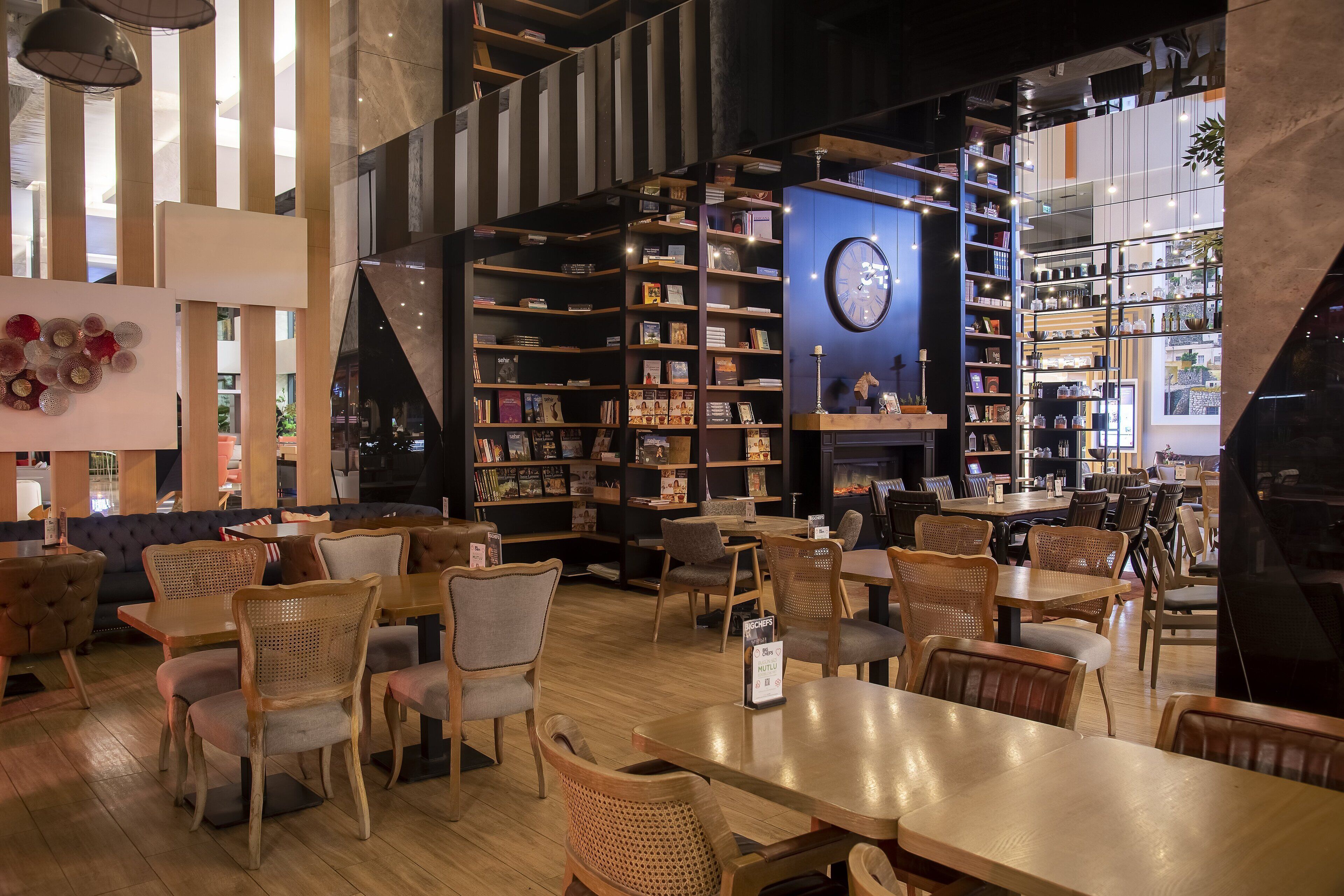 A cozy cafe with wooden furniture, a large bookshelf, and a clock on the wall.