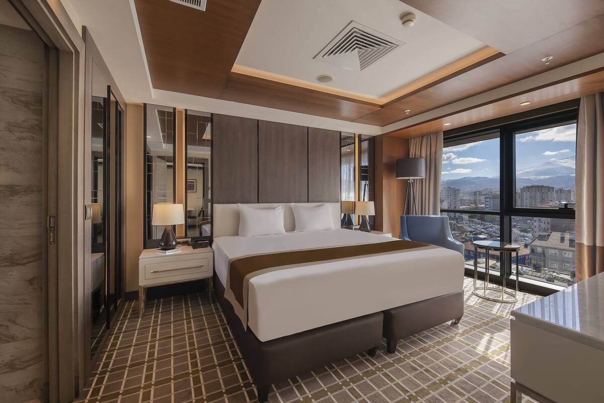 A modern hotel room with a large bed, a desk, and a view of the city.