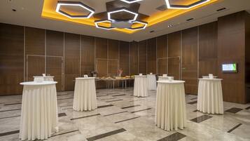 Une salle de conférence moderne, dotée de tables rondes, d’un écran central et d’un mur recouvert de panneaux en bois.