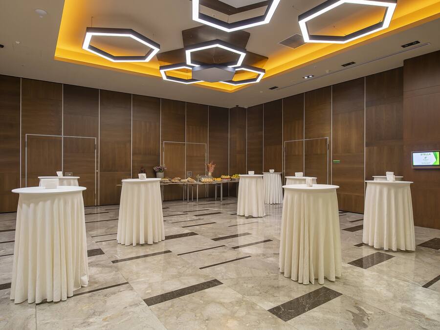 Une salle de conférence moderne, dotée de tables rondes, d’un écran central et d’un mur recouvert de panneaux en bois.