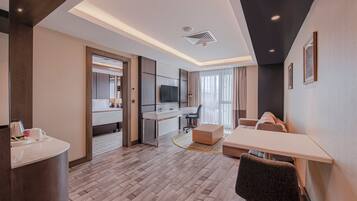 A modern hotel room with a dining area, a TV, a desk, and a sofa.