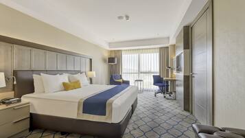A hotel room with a large bed, bedside tables, a desk, a chair, a TV, and a wardrobe.