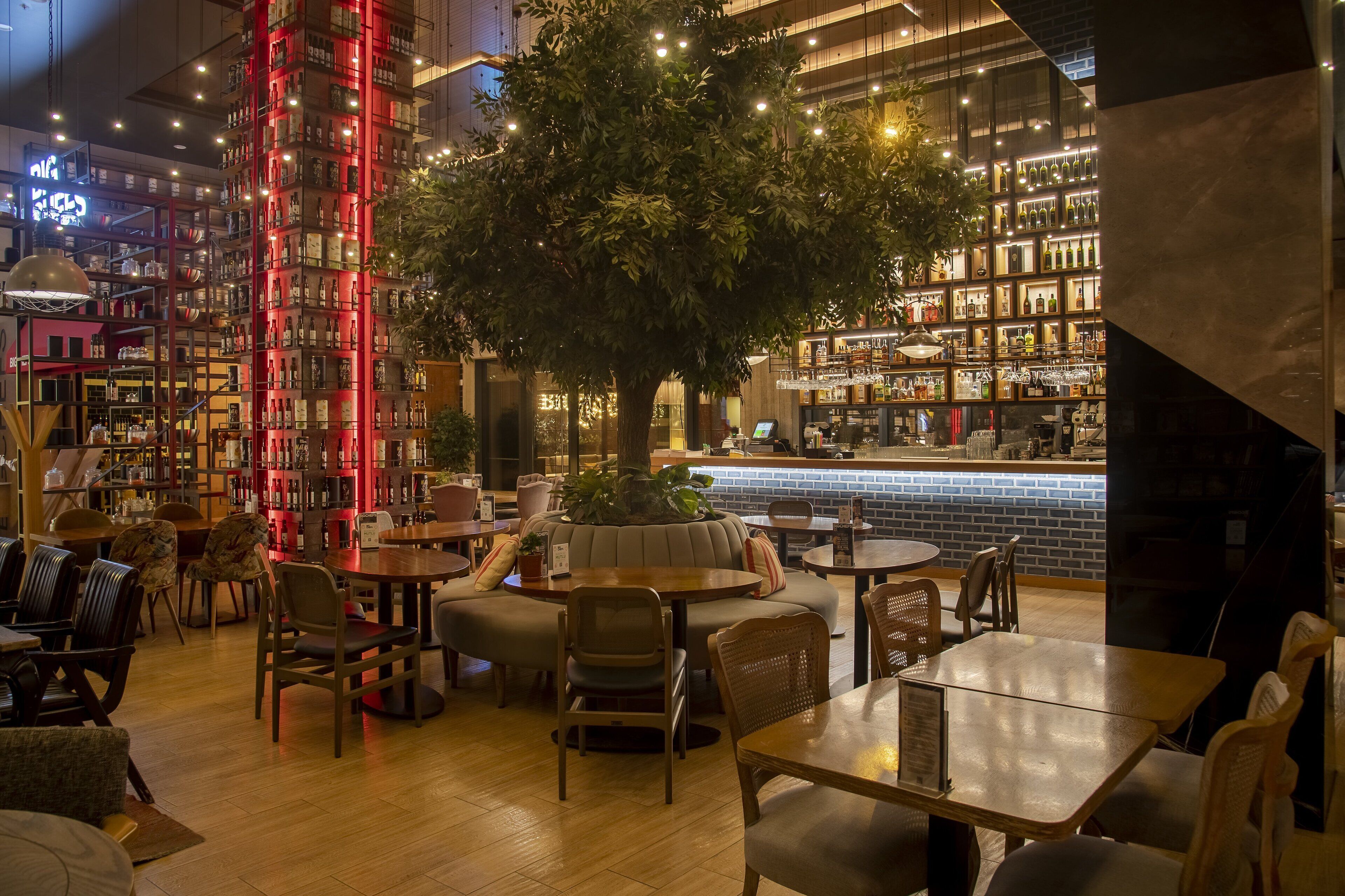 Eine moderne Bar mit einem großen Baum, Holztischen und -stühlen.
