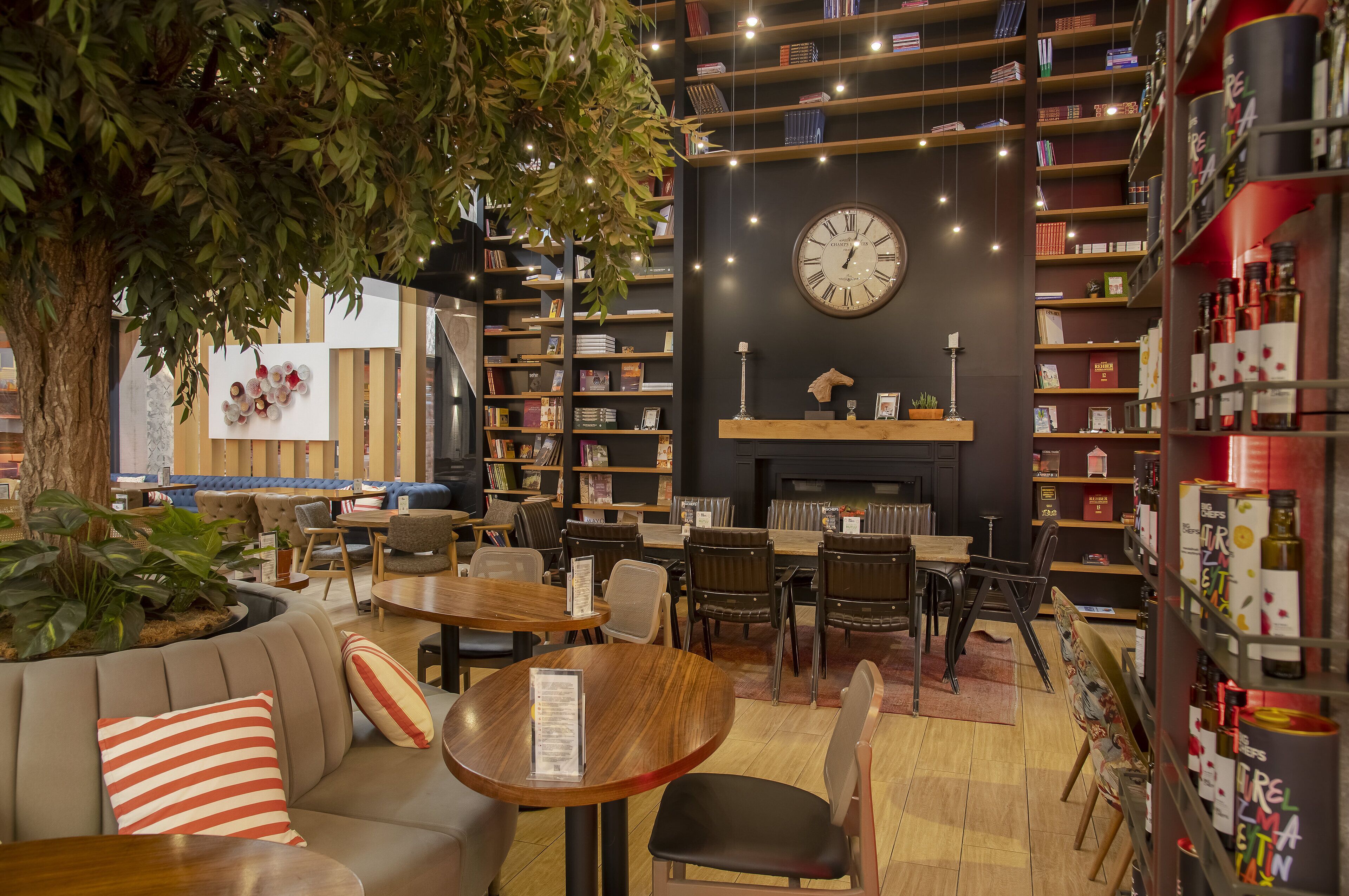 Een gezellige binnenruimte met een grote boekenkast, een ronde tafel en een bank met gestreepte kussens.