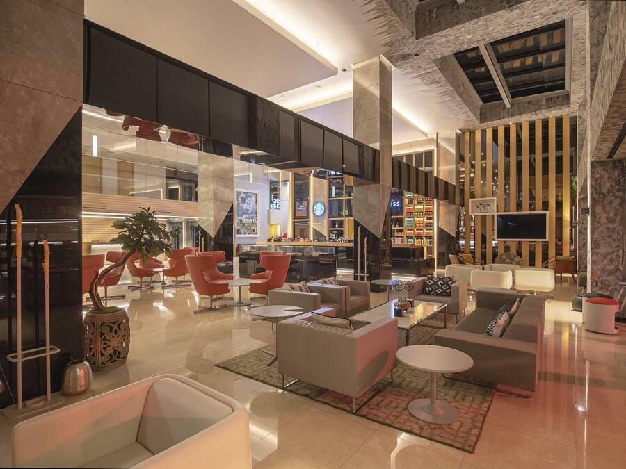 Eine moderne Lobby mit verschiedenen Sitzbereichen, einer zentralen Treppe und einer sichtbaren Bar.