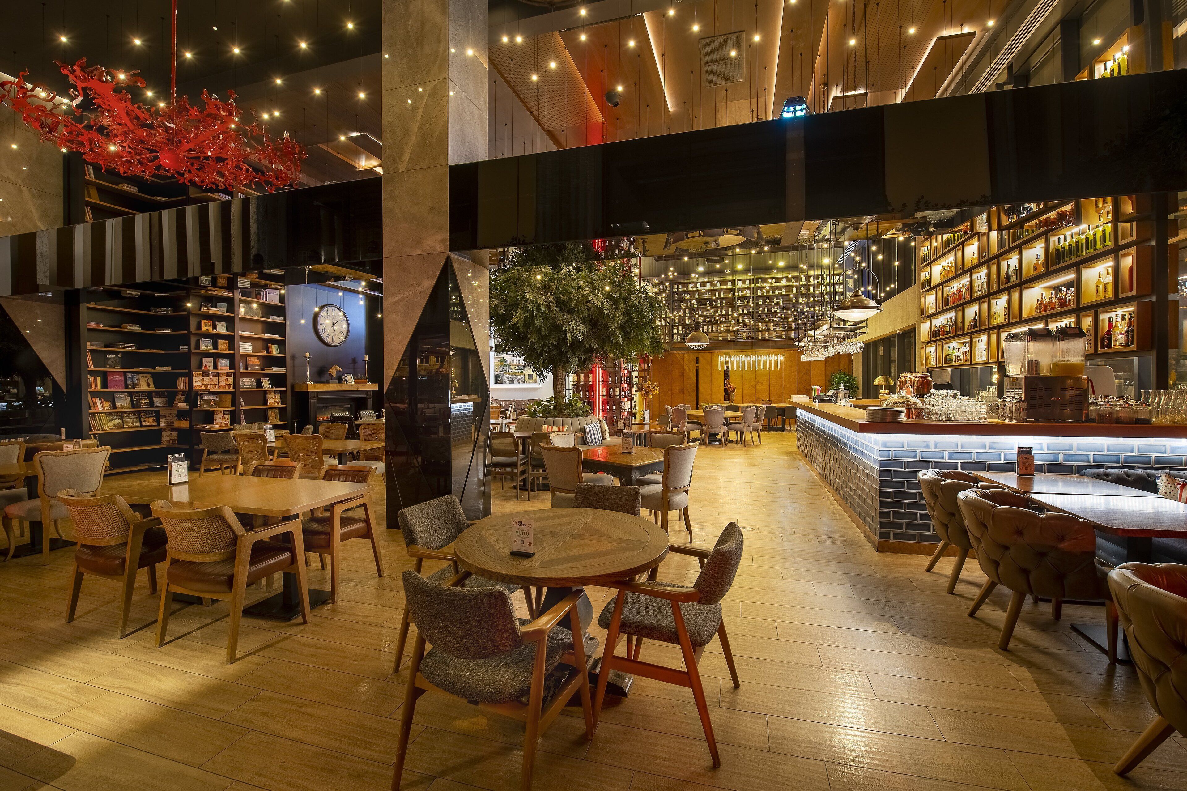 Ein modernes Interieur mit Holzboden, runden Tischen und Stühlen, einer Bar mit Flaschenregalen und einem großen, roten dekorativen Objekt an der Decke.