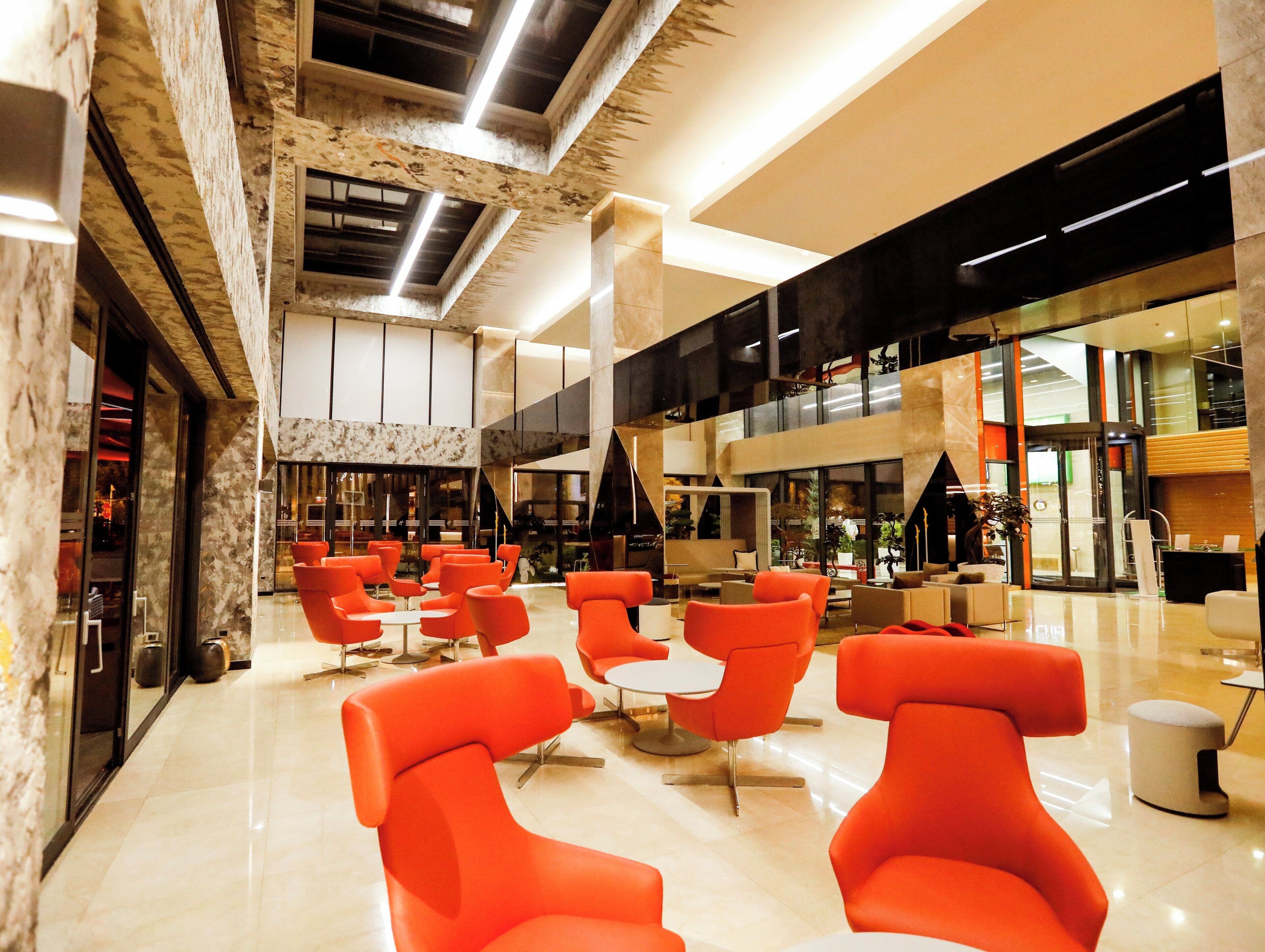 A spacious lobby with modern orange chairs, a marble floor, and a high ceiling with exposed beams.