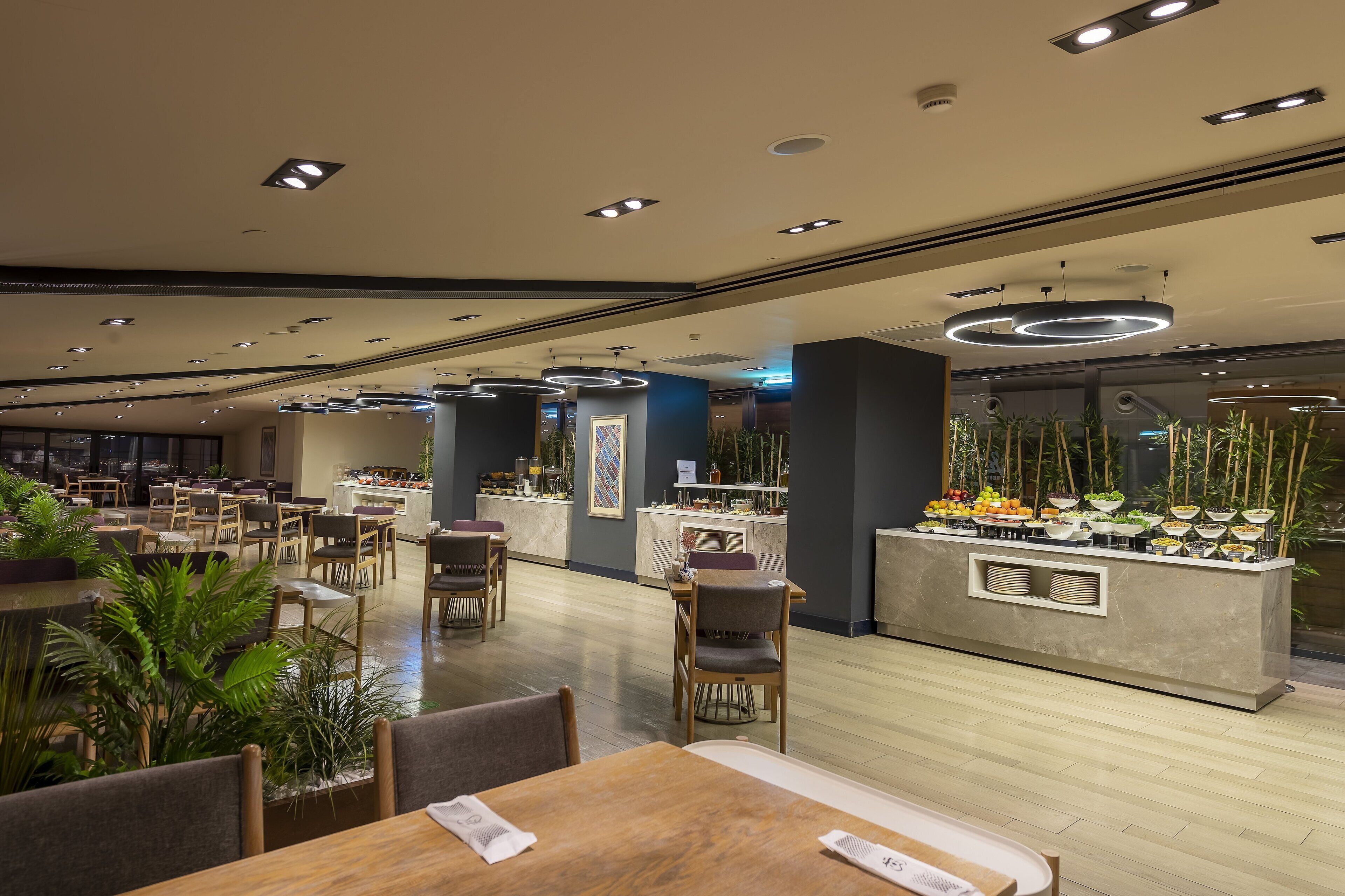 Een moderne eetruimte met meerdere tafels en stoelen, een buffet met diverse gerechten, en een receptiebalie.