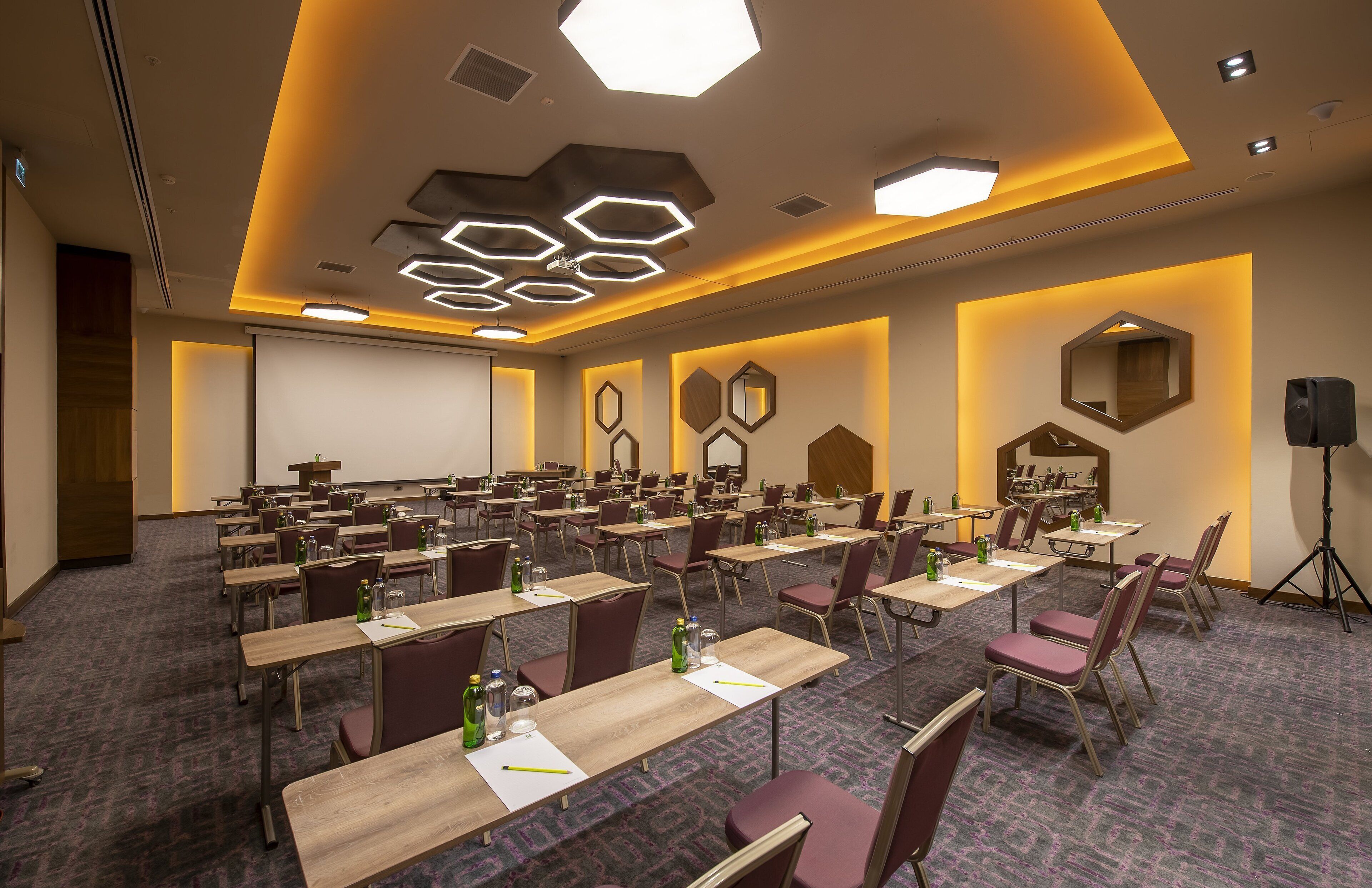A conference room with hexagonal ceiling lights, multiple tables with chairs, and a large mirror on the wall.
