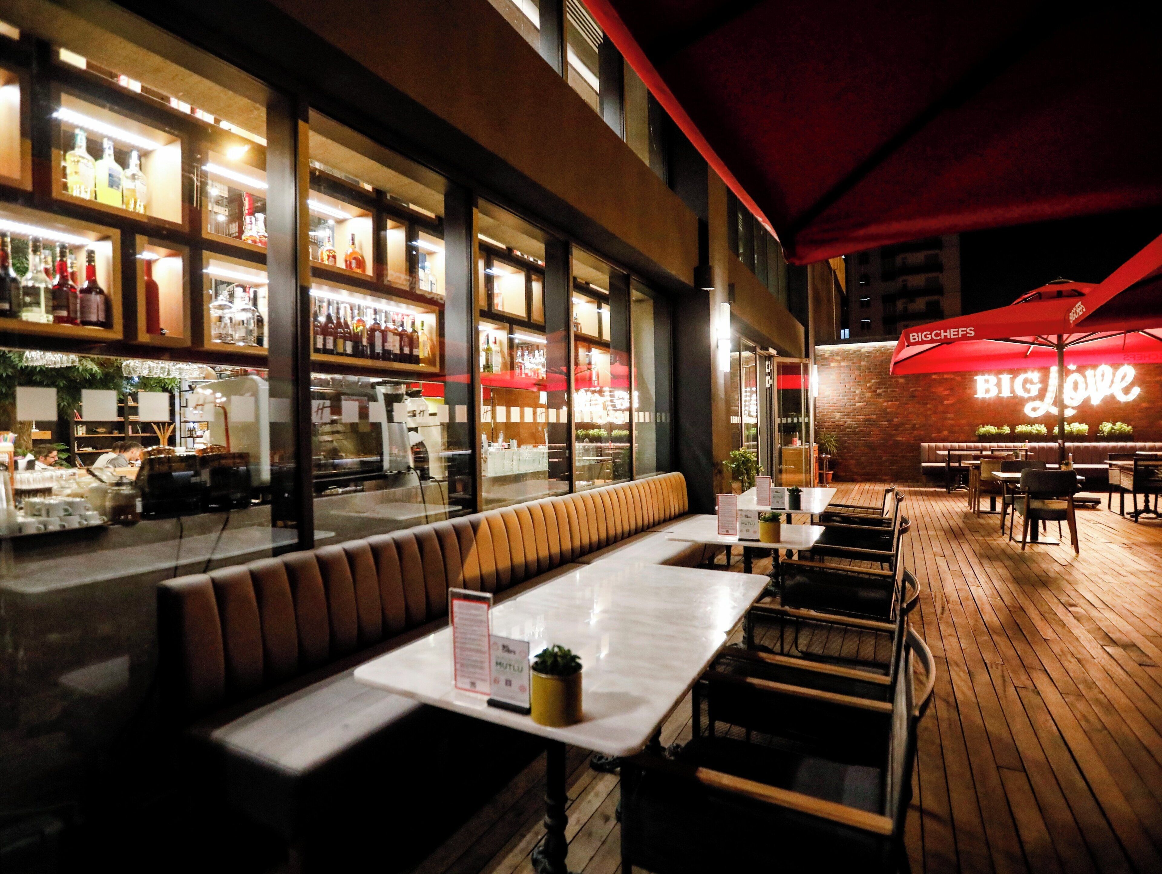 An outdoor dining area with wooden tables and benches, a brick wall, and a neon sign reading 'BIG Love'.