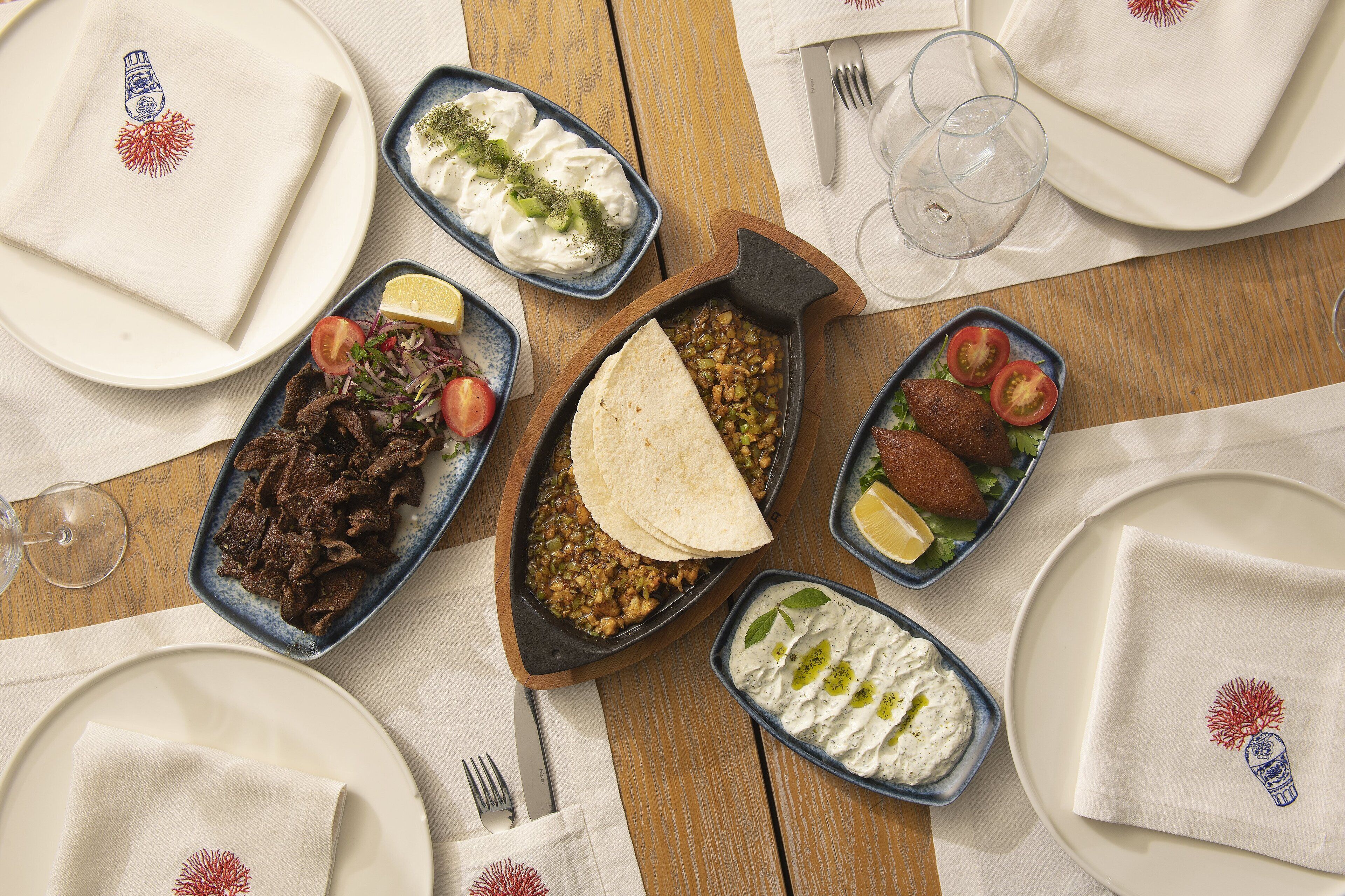 Una mesa servida con varios platos, incluyendo un cuenco de hummus, un plato de carne y un recipiente con pan plano.