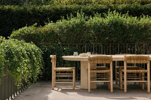 A wooden table with chairs, set outdoors with a hedge in the background.