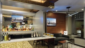 Un área de bar moderna con una encimera de mármol, repleta de botellas y vasos, y un televisor que muestra una vista urbana.
