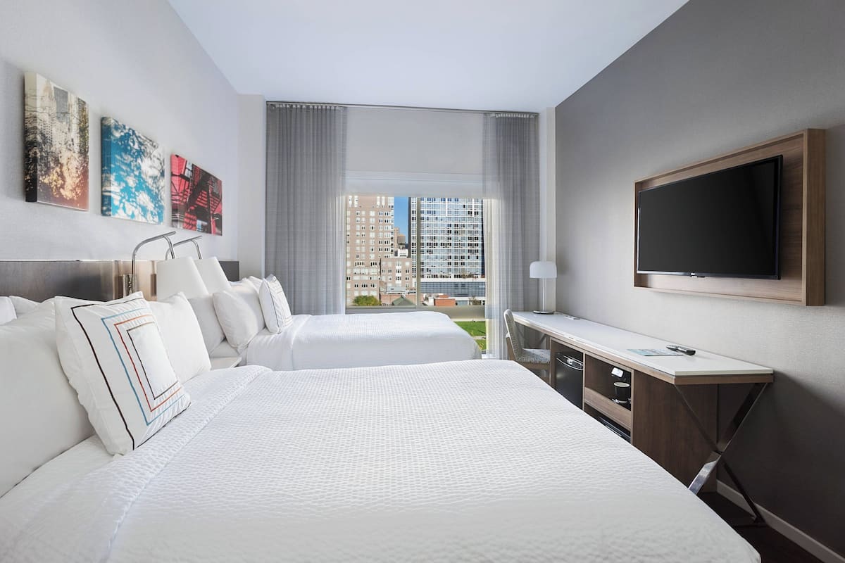 Une chambre d’hôtel avec deux lits, un bureau, une télévision et une vue sur la ville.