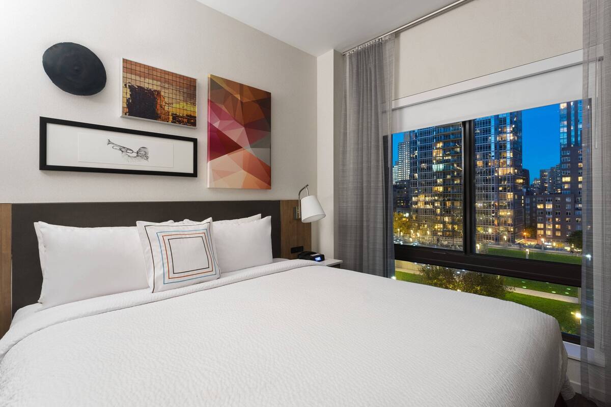 Une chambre d’hôtel avec un grand lit, une vue sur la ville et des œuvres d’art accrochées au mur.