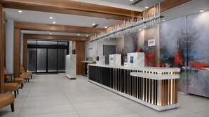 Un área de recepción moderna con un mostrador de mármol, un quiosco de información digital y un cuadro abstracto de gran tamaño en la pared.