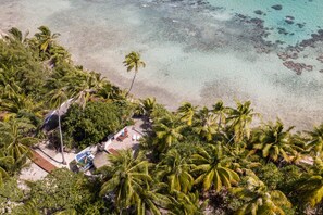 An aerial view of a tropical beach with palm trees, clear water, and a small pool area.