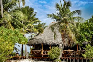 A thatched-roof structure with wooden railings, surrounded by palm trees and a clear sky. - Ninamu Resort (Tikehau)