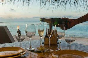 A table set for a meal with empty plates, glasses, and a bottle being poured. - Ninamu Resort (Tikehau)