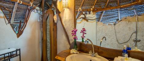 A bathroom with a wooden sink, a mirror, a shower, and a thatched roof.