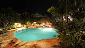 A swimming pool surrounded by palm trees and a well-lit patio area.