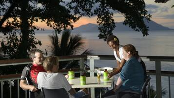 Un grupo de personas sentadas en una mesa al aire libre, con una vista panorámica de un cuerpo de agua y montañas al fondo.