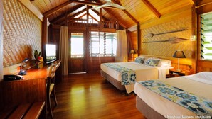 A wooden cabin room with two beds, a desk, and a ceiling fan.