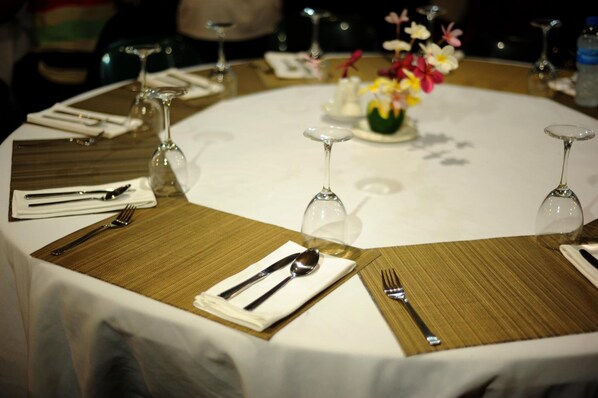 Una mesa redonda de comedor con mantel blanco, adornada con individuales dorados, cubiertos y copas de vino.