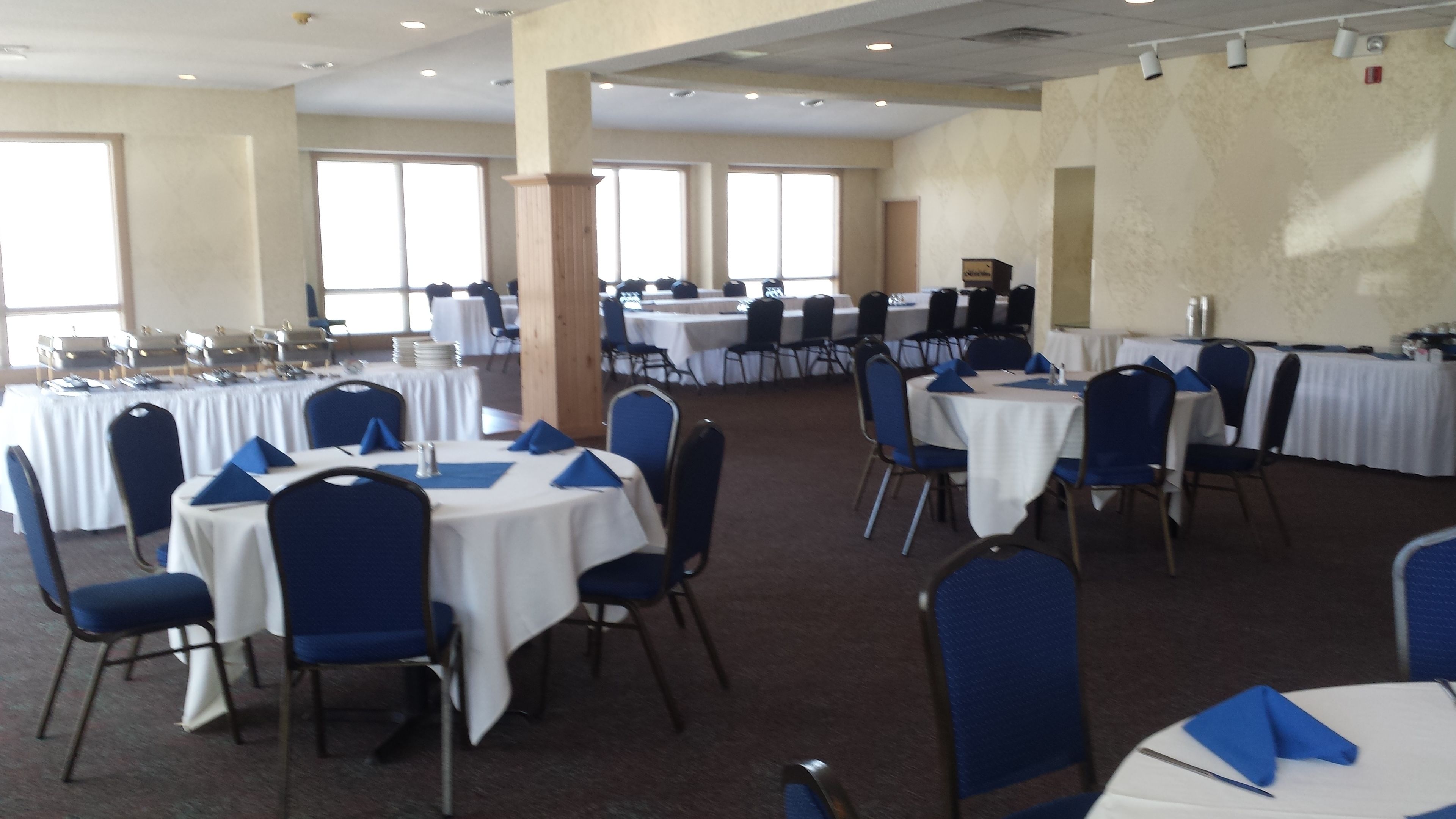 A banquet hall with round tables, blue chairs, and white tablecloths.