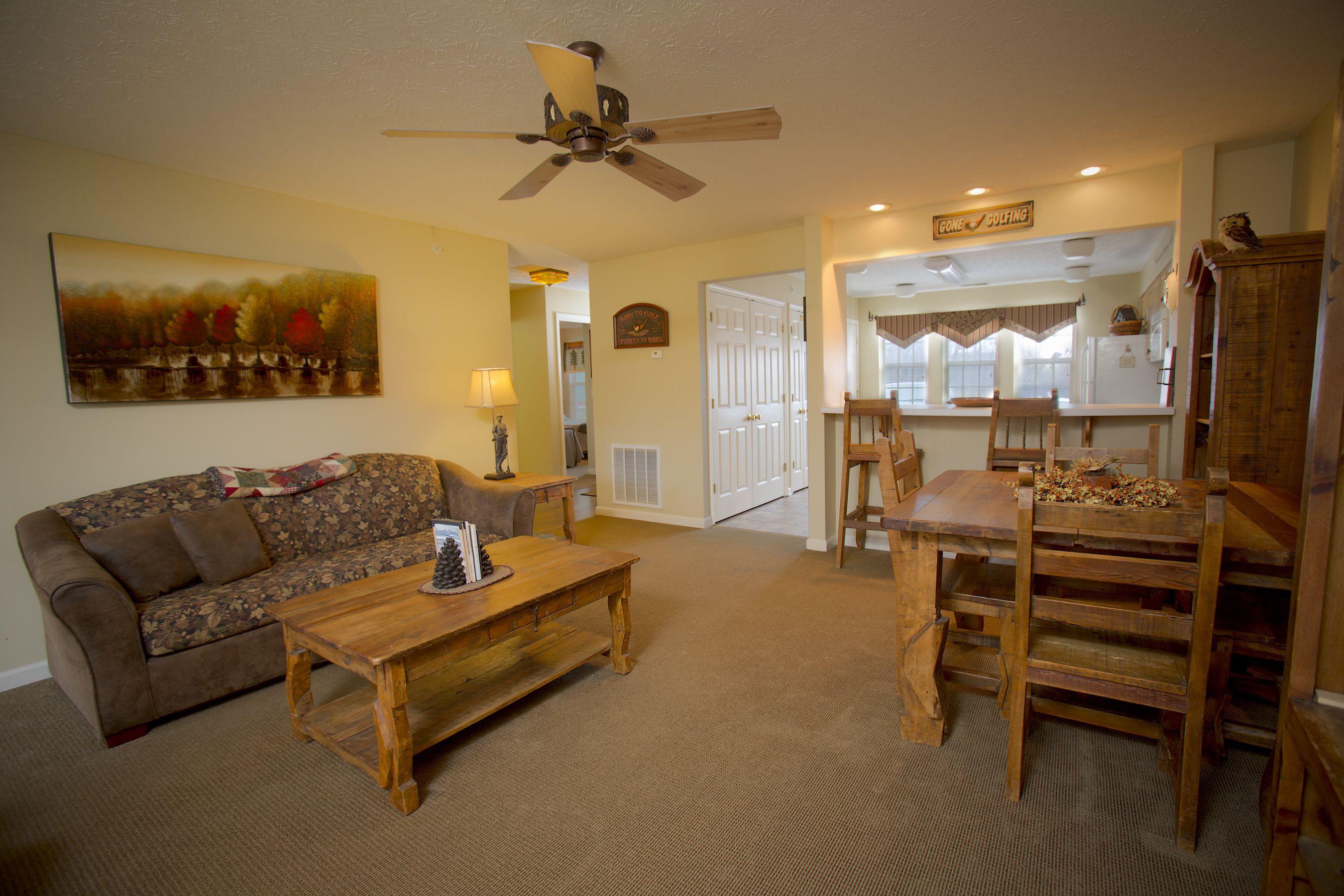 A living room with a wooden coffee table, a sofa, a ceiling fan, and a dining area with wooden chairs and a table.