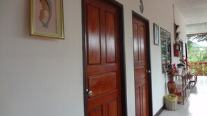 A hallway with wooden doors, a framed picture, and a fire extinguisher on the wall. - Palm House white building (Mae Hong Son)