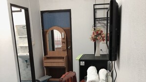 A dining area with a wooden table, chairs, a TV, and a small shelf with toiletries. - Palm House white building (Mae Hong Son)