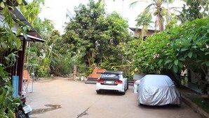 A covered car parked in a driveway with a house and lush greenery in the background. - Palm House white building (Mae Hong Son)