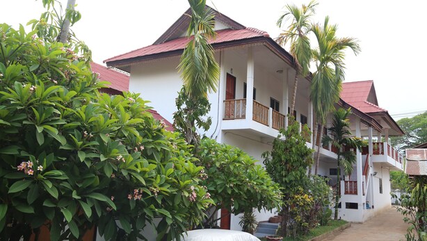 A multi-story building with balconies, surrounded by lush greenery and palm trees. - Palm House white building (Mae Hong Son)