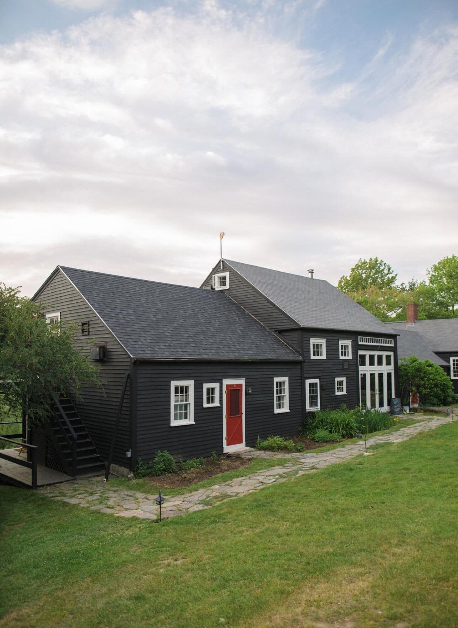 A two-story building with a dark exterior, a red door, and a small window.