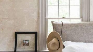 A bedroom with a bed, a window, a picture frame, and a hat on the bed.