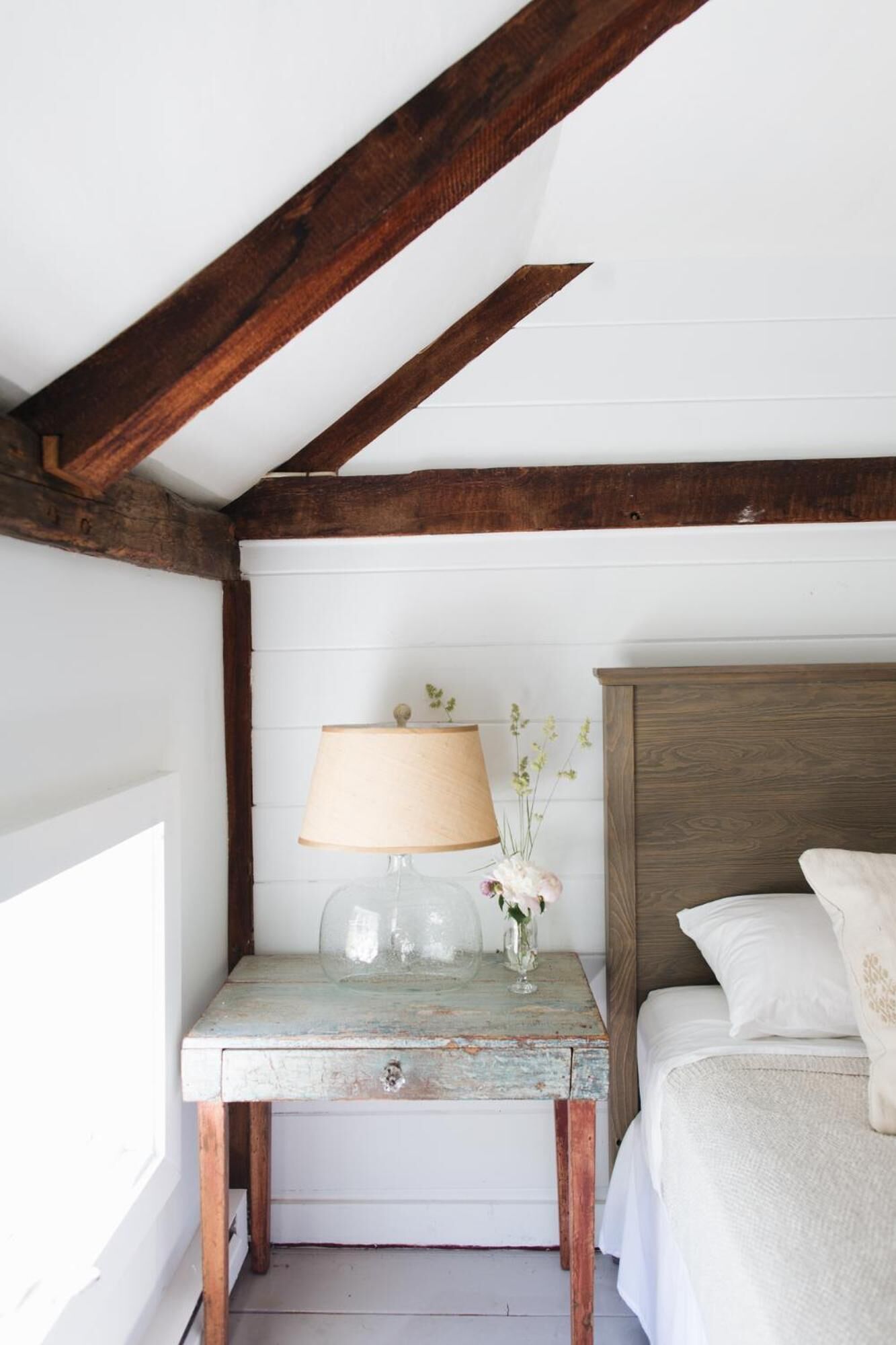 Un dormitorio con cabecera de madera, una mesita de noche con lámpara y una cama con ropa blanca.