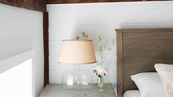 Un dormitorio con cabecera de madera, una mesita de noche con lámpara y una cama con ropa blanca.