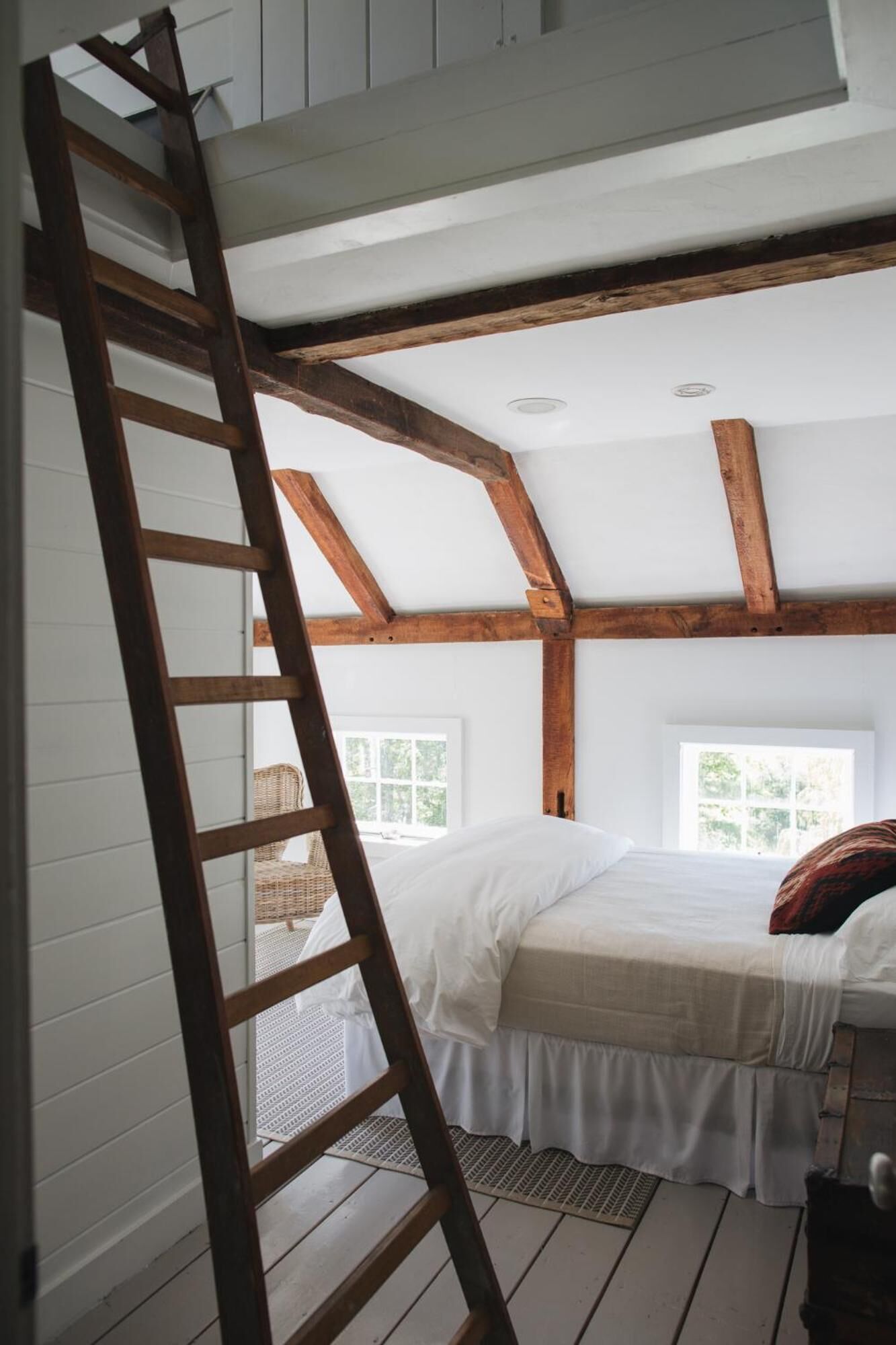 A loft bedroom with a wooden ladder, a bed, and a window.