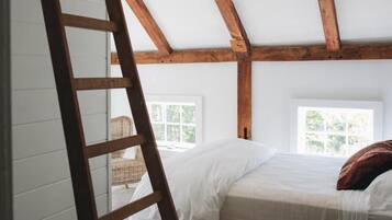 A loft bedroom with a wooden ladder, a bed, and a window.