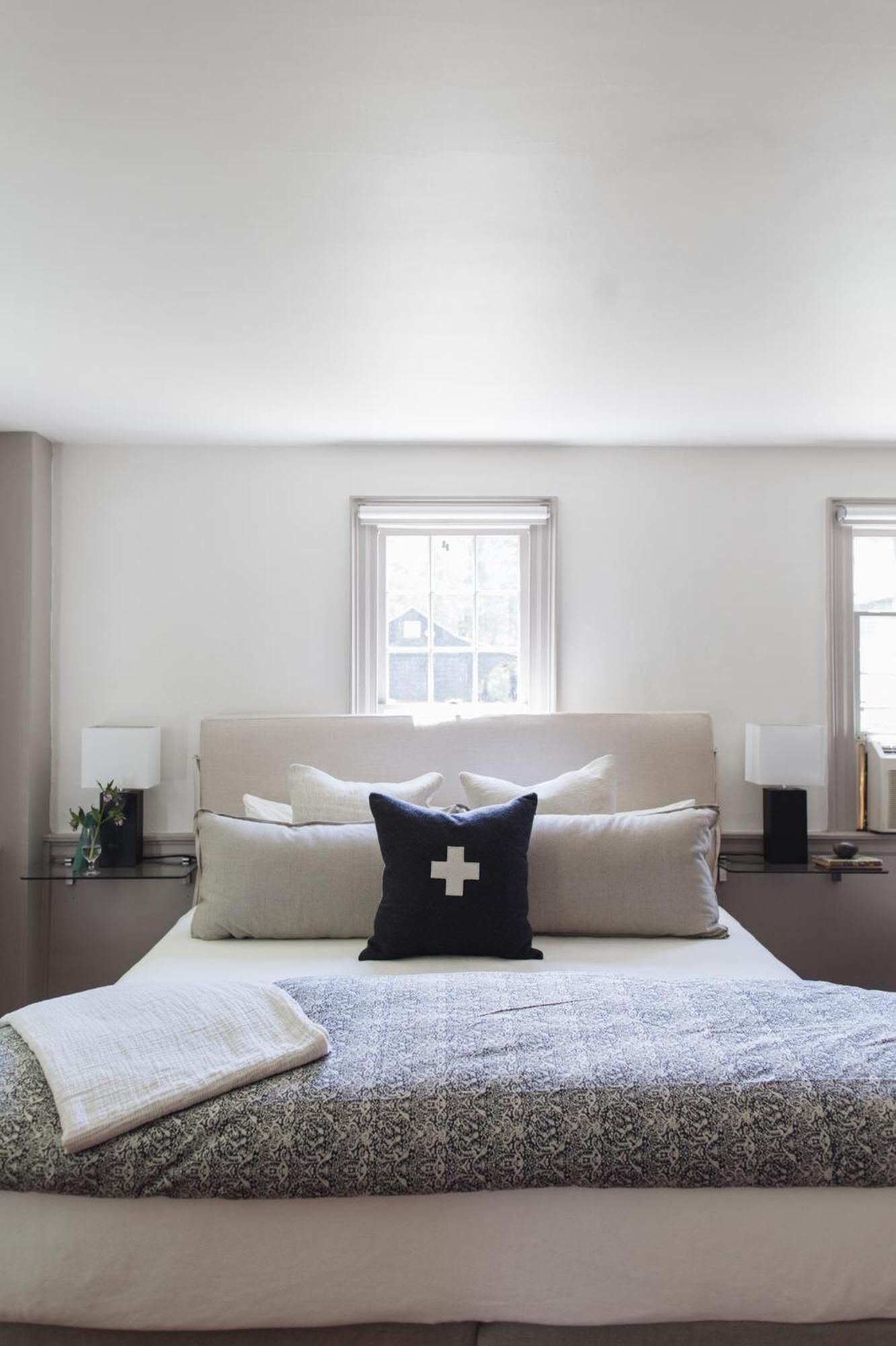 A bedroom with a large bed, two bedside tables, a window, and a nightstand with a lamp.