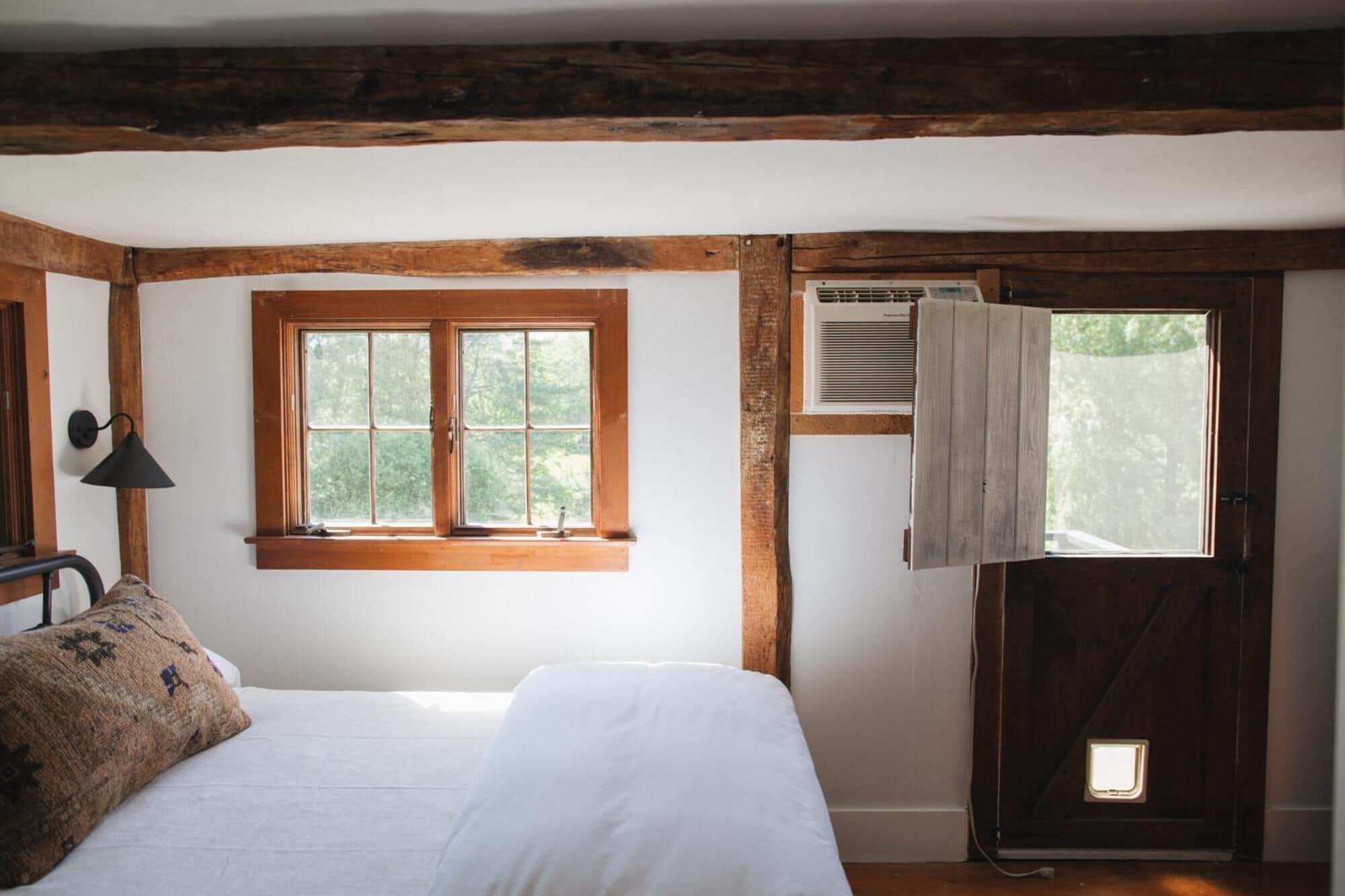 A bedroom with a bed, a window, and a door with an air conditioning unit.